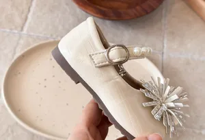 Detail shot of girls pearl rhinestone leather flat shoes with decorative flower toe and strap.