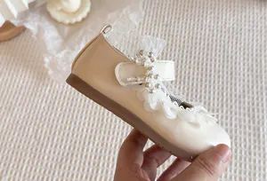 Dettaglio scarpe in pelle per bambina con finiture in pizzo, fiocco di perle e chiusura a strappo.