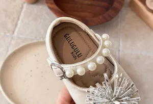 Detail of girls beige leather princess shoes featuring pearl straps and rhinestone flower.