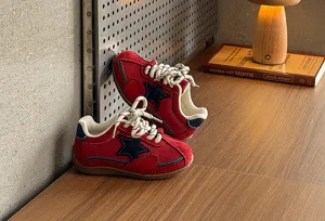 Close-up detail of retro red kids sneakers with navy star and white laces on wooden desk.