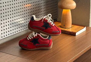Close-up of red retro kids sneakers with black star detail on wooden desk scene display.