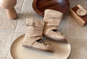 Detailed view of kids beige suede cutout boots with cute bow and buckle strap design.