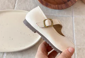 Primer plano detallado de bonitos zapatos Mary Jane para niña en marfil con hebilla metálica retro.