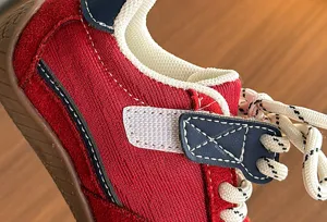Close-up of kids retro sneaker, red fabric upper with blue leather trim and white laces.