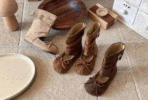 Detailed view of stylish suede girls split-toe boots with cute bow and retro wooden props.