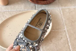 Détail de chaussure fille à paillettes grises avec finition brillante et bride.