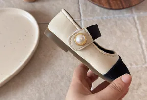 Gros plan sur les détails des chaussures Mary Jane bicolores pour filles avec perle élégante.