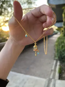 Detailed view of Tibetan style gold enamel prayer wheel pendant necklace with turquoise stones.