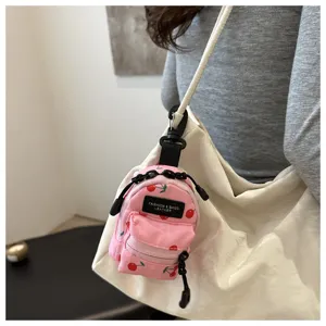 Detailaufnahme des kleinen rosa Kirschen Rucksack Anhängers an einer weißen Handtasche.