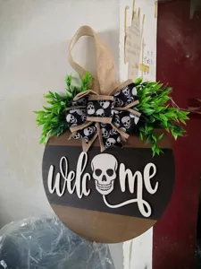Halloween wooden skull welcome door sign detail, rustic burlap bow and green foliage hanging.