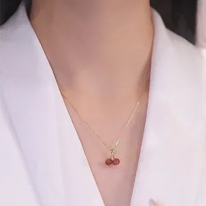Close-up detail of delicate gold clavicle chain with cute red garnet cherry pendant.