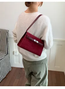 Detalle de bolso de hombro de ante burdeos, elegante bolso con cierre de vuelta metálico.