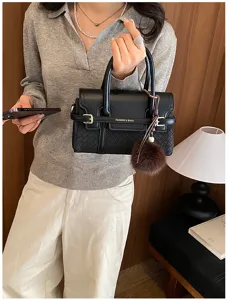 Chic black woven leather handbag with top handle, metal buckle, and cute pom-pom charm.