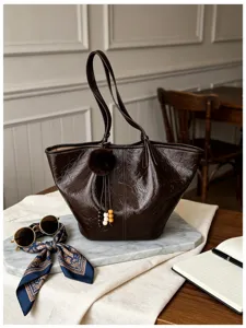 Detailed close-up of brown crinkled leather shoulder bag with furry charm on marble desk.