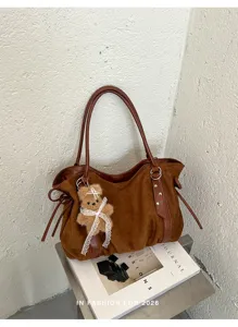 Detail view of brown suede shoulder bag featuring a cute plush bear charm and leather handles.