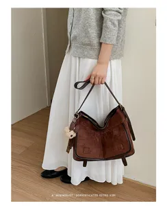 Detailed view of brown retro suede shoulder bag with chic slouchy design and cute bear charm.