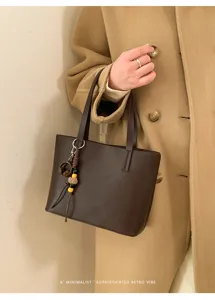 Borsa tote minimalista in pelle marrone scuro con ciondolo, ideale per tutti i giorni.