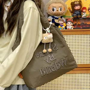 Close-up detail of casual brown shoulder bag featuring letter embroidery and plush charm.