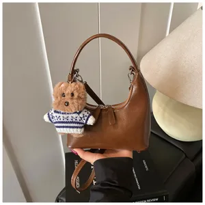 Detail view of the brown crescent shoulder bag with a cute plush bear keychain accessory.