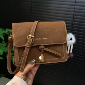 Retro brown crossbody bag detail showing fine stitching, metal hardware and fuzzy pendant.