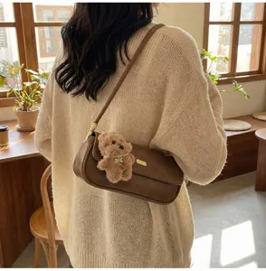 Detailed view of a stylish brown vintage baguette shoulder bag with cute plush bear pendant.