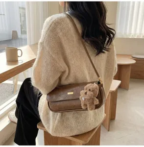 Detailed shot of trendy brown leather baguette shoulder bag with cute plush bear pendant.