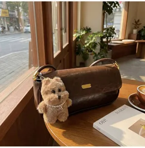 Detail view of a vintage brown leather baguette shoulder bag decorated with a cute fluffy bear pendant.