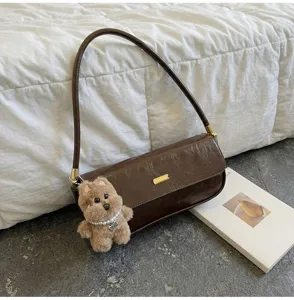 Vintage dark brown leather baguette shoulder bag detail featuring a cute fluffy bear charm.