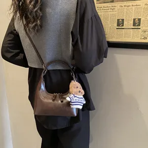 Vintage brown crescent shoulder bag for women with cute puppy plush pendant for daily commute.