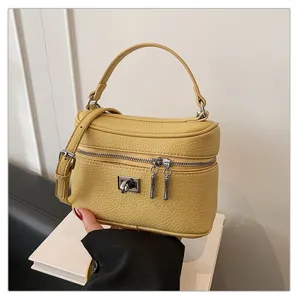 Close-up of stylish yellow leather box handbag featuring metal lock and top handle details.