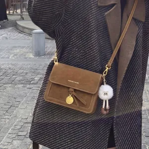 Vintage brown suede crossbody bag with metallic pendant and cute fluffy plush charm.