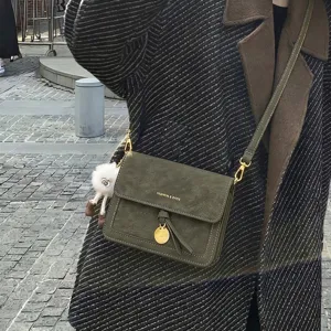 Close-up of dark green suede crossbody bag, stylish metal coin pendant and cute furry charm.