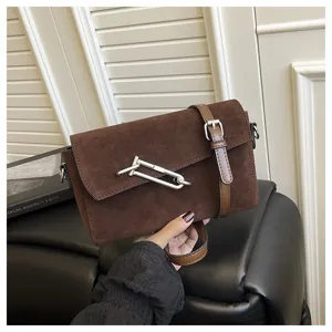 Detail shot of a stylish brown suede shoulder bag featuring a unique metal clasp and strap.