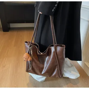 Detail view of a brown PU leather tote bag with a cute bear charm, perfect for daily commute.