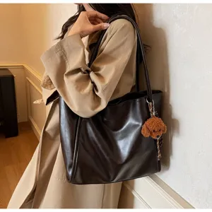 Detailed view of large capacity dark brown leather tote bag with cute plush dog pendant.