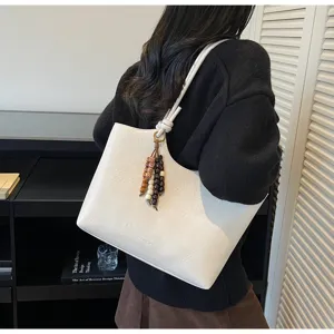 Detail shot of white leather tote bag with wooden bead pendant and comfortable shoulder strap.
