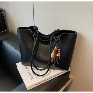 Detailed view of the black faux leather tote bag with unique knot handles and wooden beads.