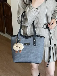 Grey textured tote bag detail, featuring black handles, plush charm, and daily commuting style.