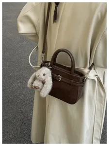 Detail shot of the brown leather handbag featuring a cute plush bunny charm and shoulder strap.