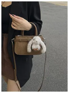Detailed close-up of brown suede crossbody handbag featuring a cute fluffy bunny plush pendant.