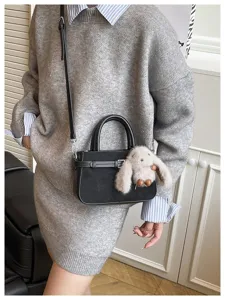 Close-up detail of the black handbag with belt buckle and cute plush bunny charm pendant.