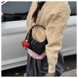Detailed view of a chic black crescent shoulder bag with cute fluffy charms worn outdoors.