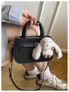 Detail view of stylish black handbag featuring a cute plush bunny charm and shoulder strap.