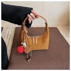 Close-up of brown suede hobo bag with tassel charm and dual zipper, showing soft texture.