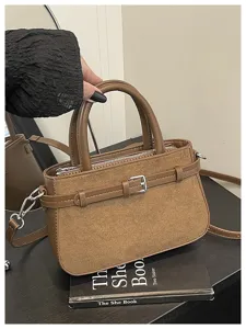 Detailed shot of brown suede handbag with decorative buckle handle and strap on dark table surface.