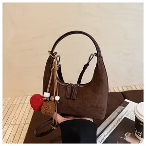 Brown suede hobo handbag detail showing soft texture, dumpling shape and cute pom pom charms.