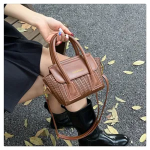 Detalle de bolso de mano tejido marrón, elegante bolso cruzado con asas y diseño de solapa.