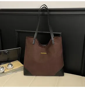 Detail view of brown suede tote bag with black leather straps and chic gold bar decoration.