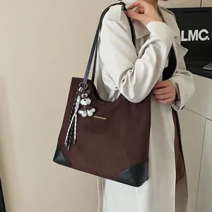 Detailed view of the large brown suede tote bag with black corner trim and cute dog charm.