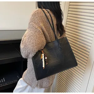 Detailed view of a black PU leather tote bag with shoulder straps and wooden bead charm.